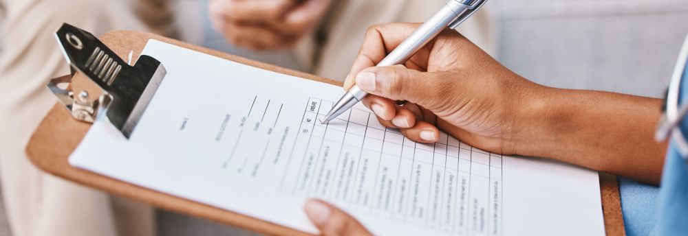 A hand holds a pen over a clipboard and begins to fill out a box on the paper.